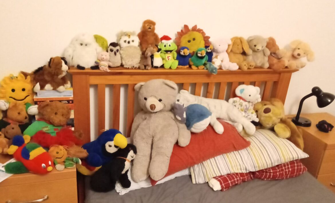 An image showing the front end of Jorik's bed, with a variety of cuddly toys along the headboard and on top of the pillows. It looks pretty dang comfortable.