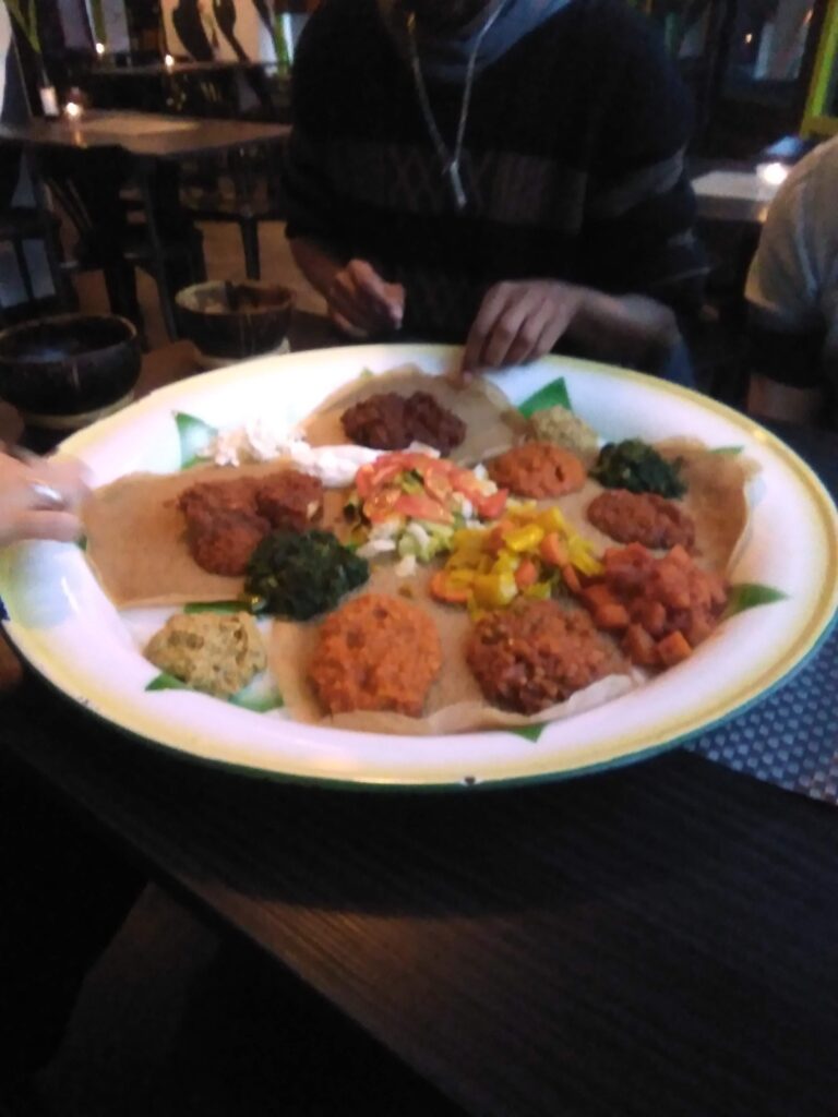 An image of the incredible Ethiopian meal we had in Amsterdam. You see a large plate with a variety of dishes on top of sorghum flatbreads.